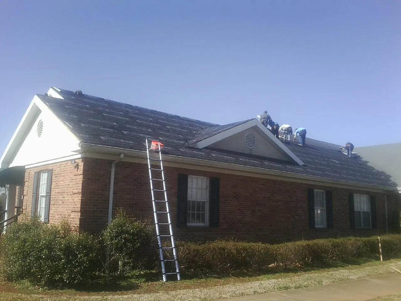 Crew tearing shingles off a brick ranch roof with a ladder set — Metal Roof Repair work by our crew in Albrightsville