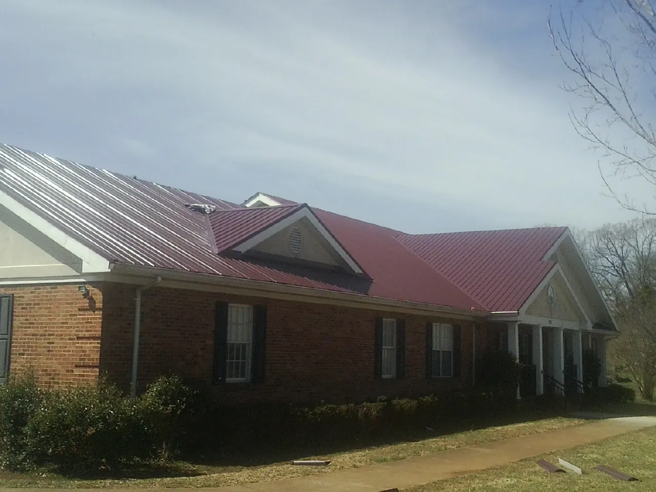 Red metal roof with gabled entries on a long brick building, from a Hail Damage Roof Repair job in Albrightsville