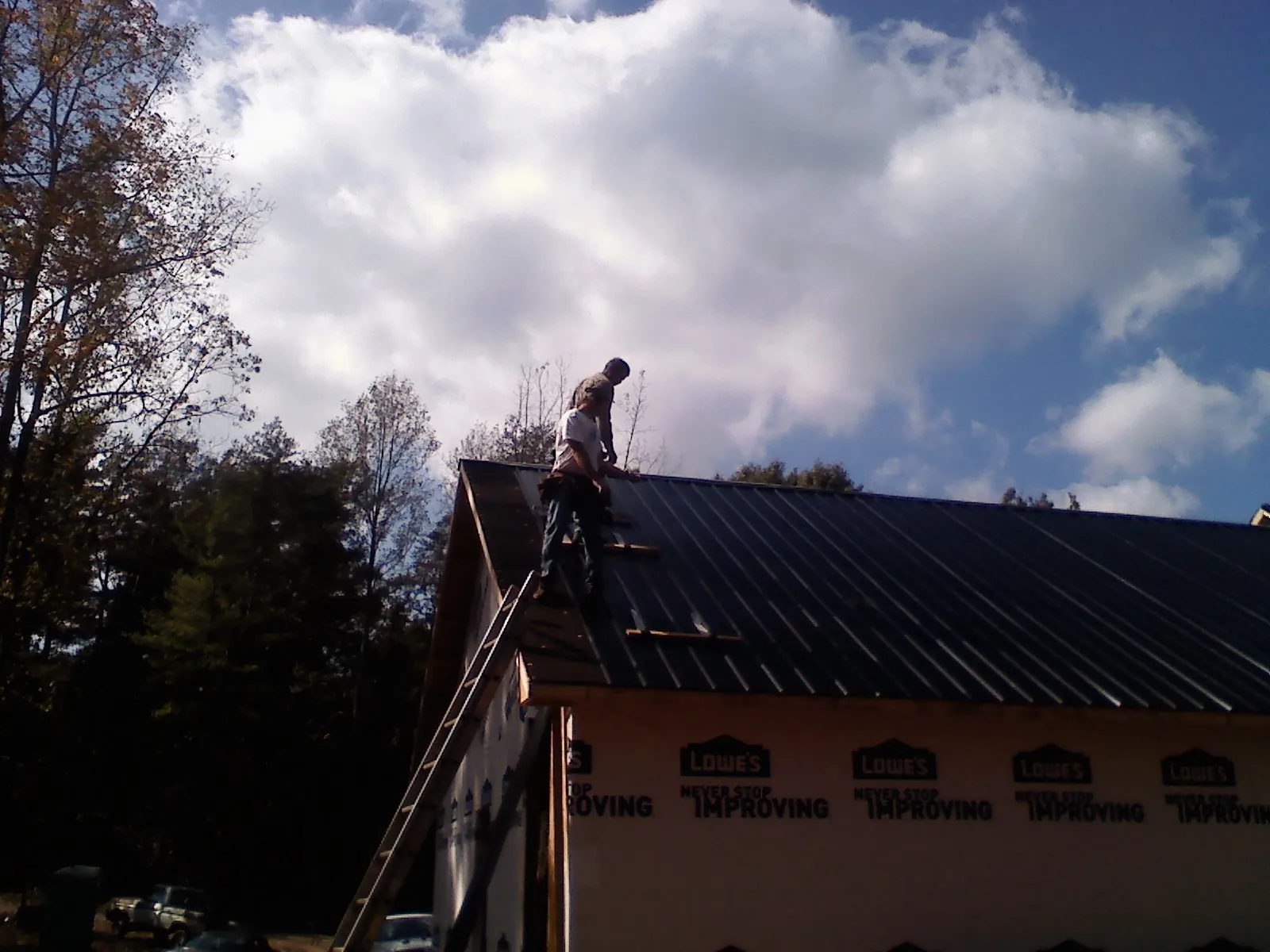 Roofer fastening dark metal panels high against a cloudy sky, from a Roof Inspection job in Albrightsville