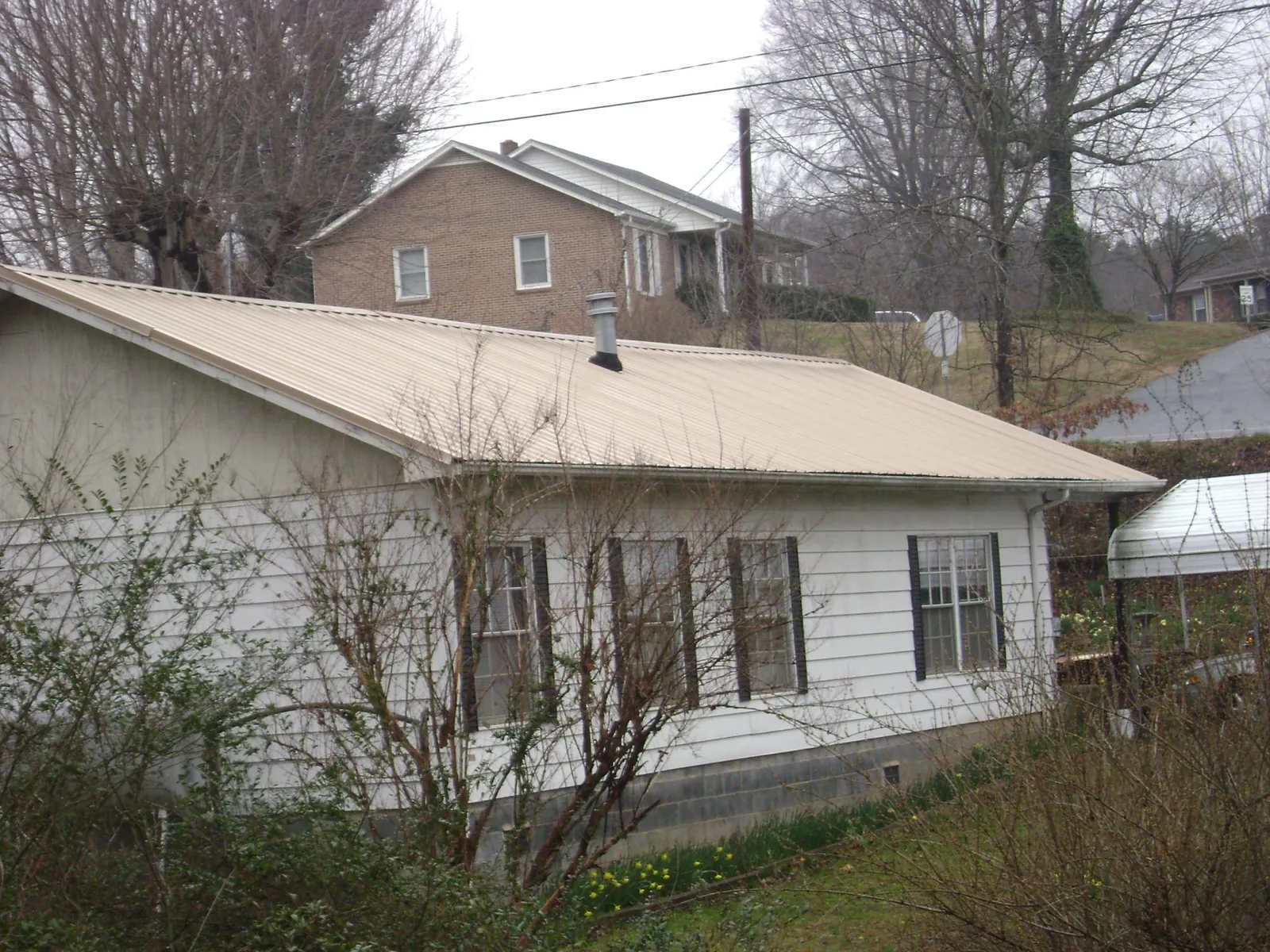 Tan metal roof on a white sided house set into a hillside — Commercial Roofing by Roofing Brothers in Albrightsville
